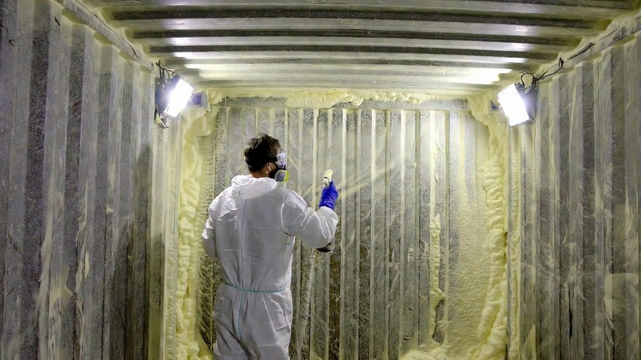 Worker applying closed-cell spray foam insulation inside a shipping container